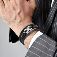 Bracelet multi-rangs en cuir noir avec motif infini en métal argenté porté au poignet.