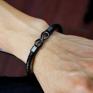 Bracelet en cuir noir tressé avec ornement infini noir brillant, modèle Yanis, porté au poignet.