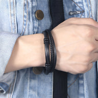 Bracelet en cuir noir tressé et lisse avec fermoir tubulaire mat sur poignet masculin.