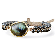 Bracelet femme avec pierre centrale labradorite irisée sertie or, perles noires tourmaline et tressage beige ajustable.