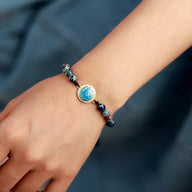 Bracelet femme avec perles de jaspe bleu et pierre centrale opale aux reflets irisés, monture dorée.
