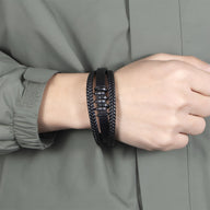 Bracelet multi-rangs noir en cuir avec motif ondulé et tresse, fermoir métallique noir.