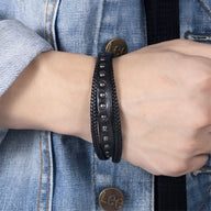 Bracelet multi-rangs en cuir noir avec rivets métalliques, style masculin, porté au poignet.