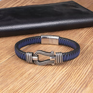 Bracelet bleu en cuir tressé avec boucle en acier argenté modèle Damien posé sur surface en bois clair.