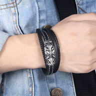 Bracelet multi-rangs en cuir noir avec détail croix en métal argenté sur poignet homme.