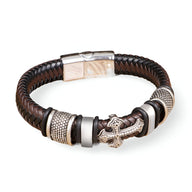 Bracelet marron en cuir tressé avec croix et détails métalliques argentés, fermoir magnétique.