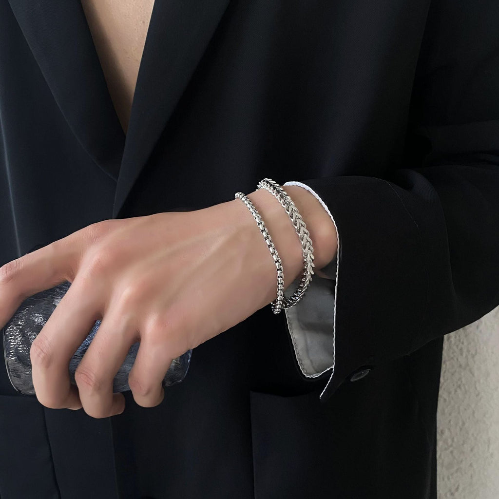 Bracelet en titane argent à double maille fine porté sur poignet masculin avec manche de veste noire.