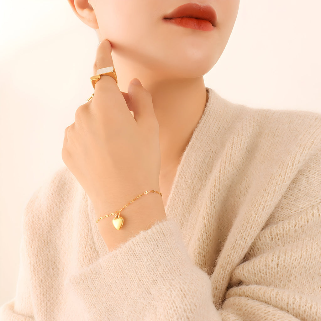 Bracelet en titane doré avec pendentif cœur discret porté au poignet féminin, style délicat et élégant.