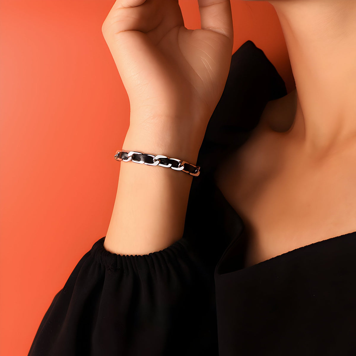 Bracelet en titane argenté avec maillons larges sur cordelette en cuir noir, porté au poignet féminin.