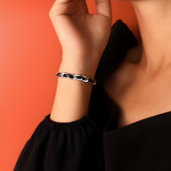 Bracelet en titane argenté avec maillons larges sur cordelette en cuir noir, porté au poignet féminin.