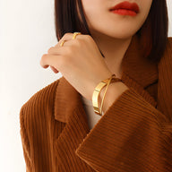 Bracelet jonc en titane plaqué or 18 carats au design entrelacé porté sur poignet féminin.