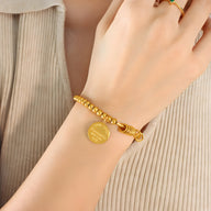 Bracelet en titane plaqué or 18 carats avec billes rondes, anneaux et médaille gravée.