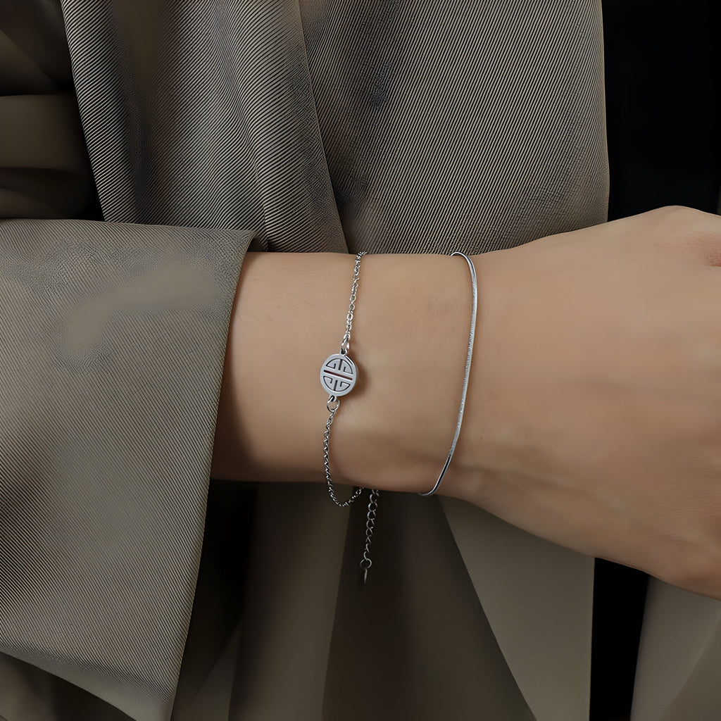 Bracelet en titane plaqué or 18 carats avec médaillon rond à motif géométrique, finition argentée, porté au poignet.