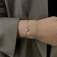 Bracelet en titane plaqué or 18 carats avec médaillon rond à motif géométrique, finition argentée, porté au poignet.