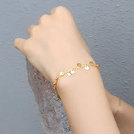 Bracelet fin en titane plaqué or 18 carats avec petits charmes ronds et brillants.