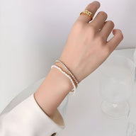 Bracelet double rangs or 18 carats avec perles blanches naturelles et zircons étincelants, porté au poignet féminin.