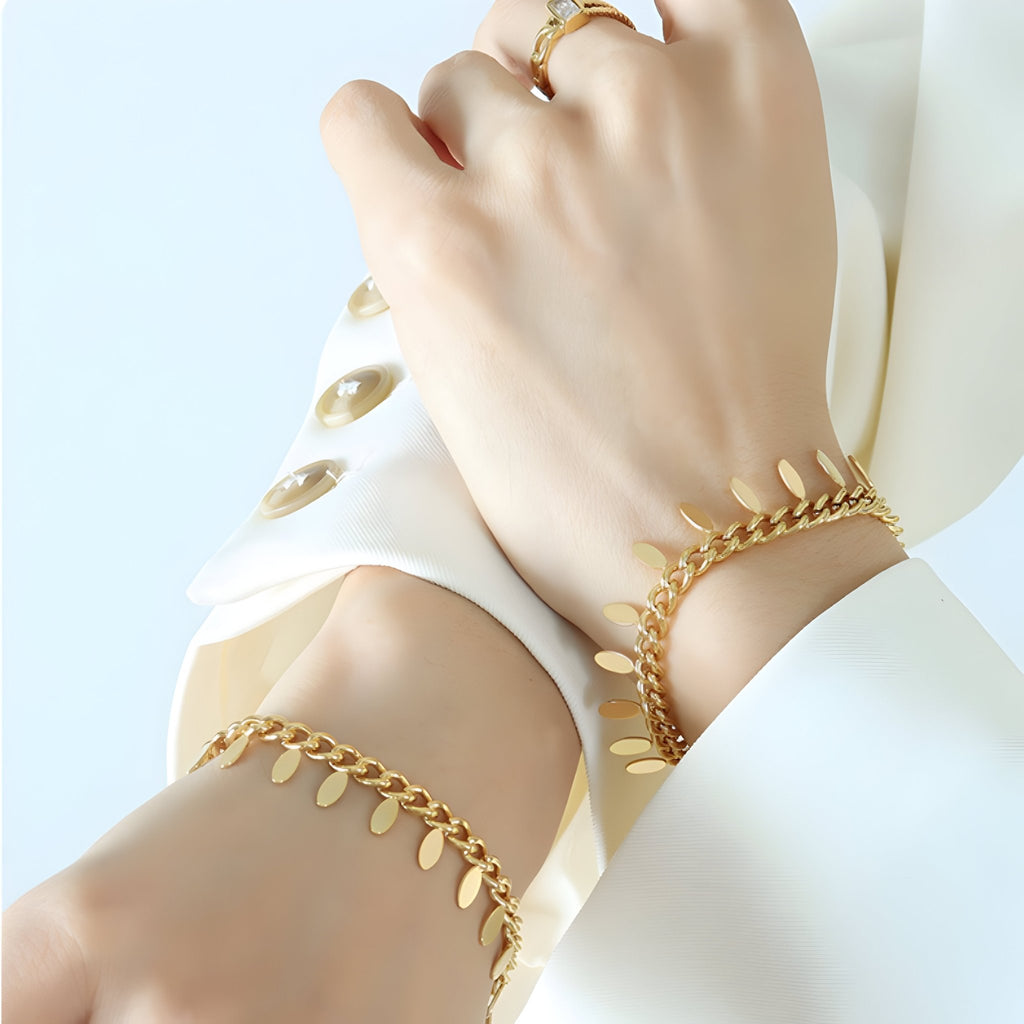 Bracelet chaînette en titane plaqué or 18 carats avec petits médaillons délicats, porté sur poignet féminin.