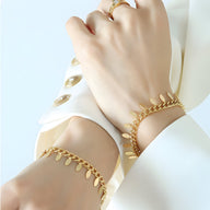 Bracelet chaînette en titane plaqué or 18 carats avec petits médaillons délicats, porté sur poignet féminin.