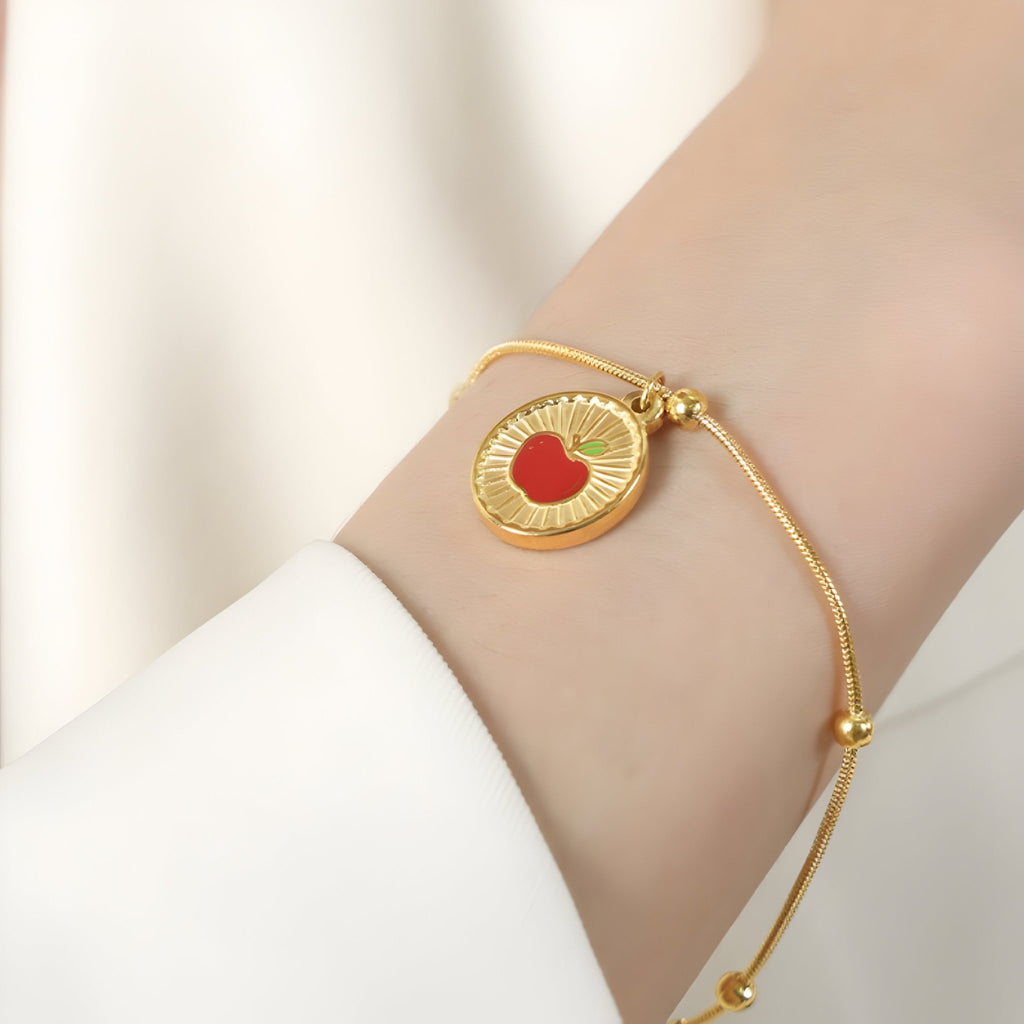 Bracelet fin en titane plaqué or 18 carats avec médaille dorée gravée d'une pomme rouge au centre.