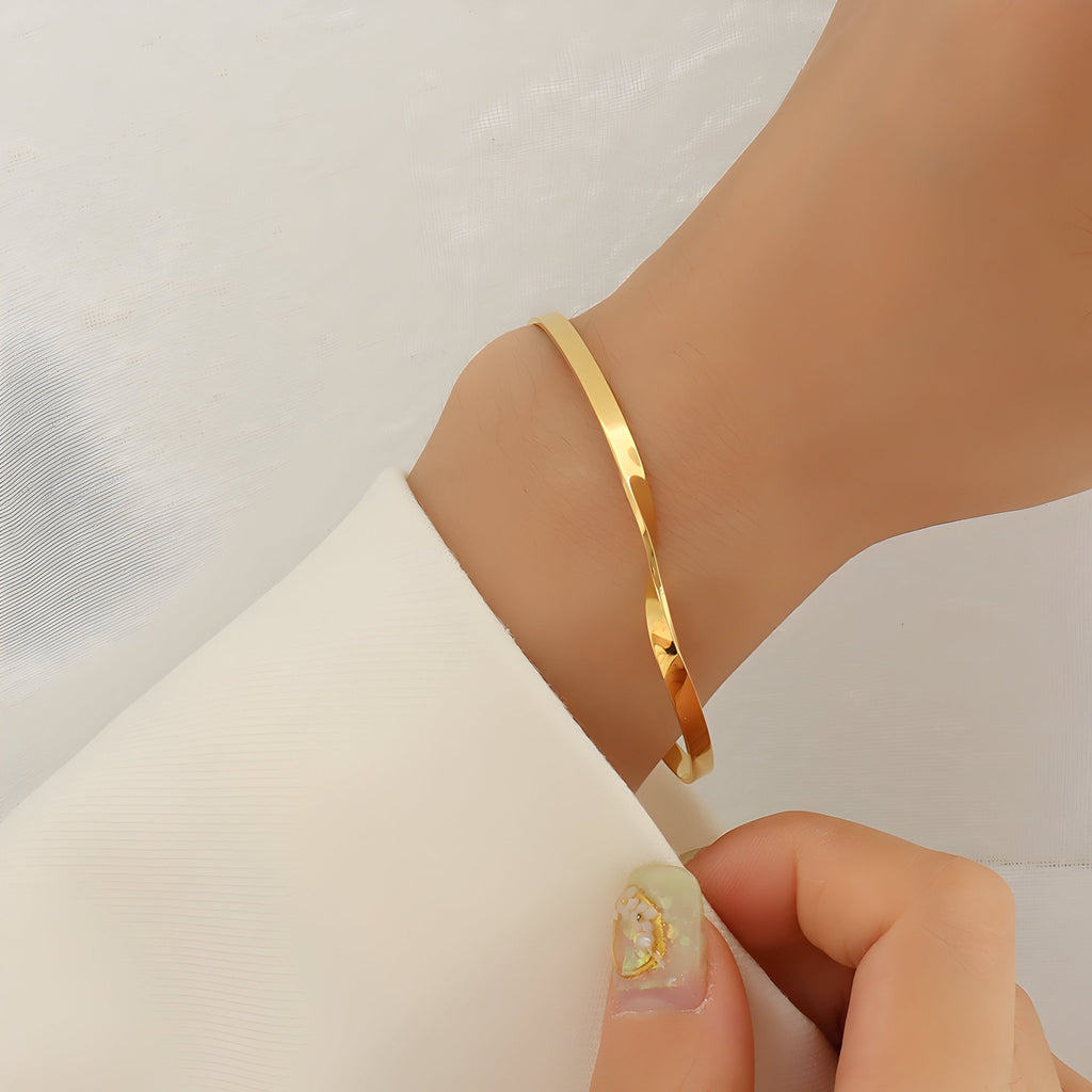 Bracelet fin en titane plaqué or 18 carats avec un design torsadé élégant porté au poignet.