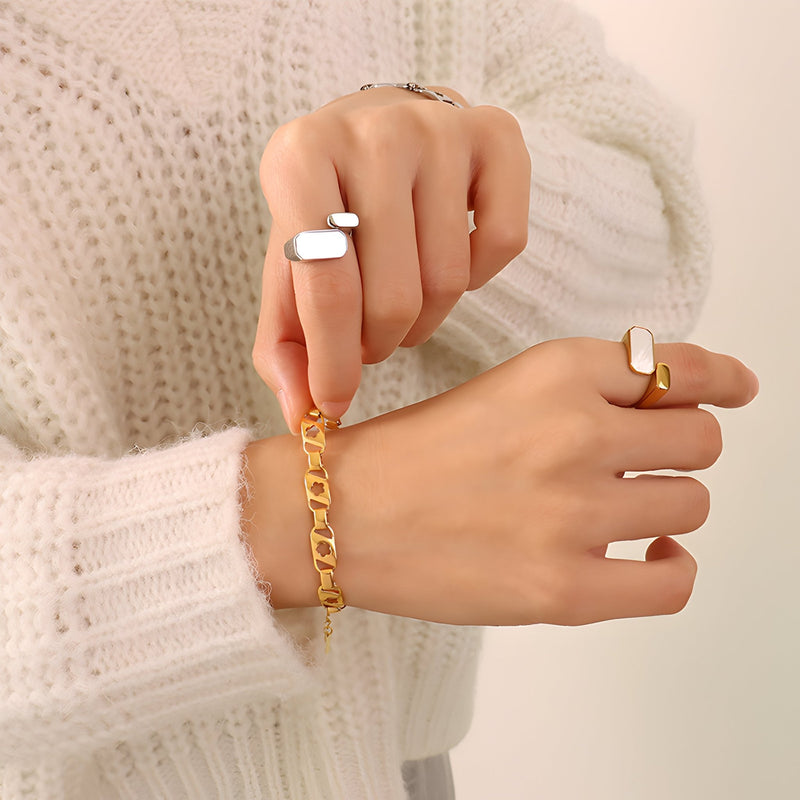 Bracelet en titane plaqué or 18 carats à maillons larges porté au poignet féminin avec pulls en maille crème.