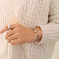 Bracelet en titane plaqué or 18 carats à maillons fins et étoiles creuses porté sur poignet féminin avec pull en maille écru.