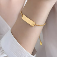 Bracelet chaîne fine en titane plaqué or 18 carats avec plaque rectangulaire lisse et fermoir ajustable.