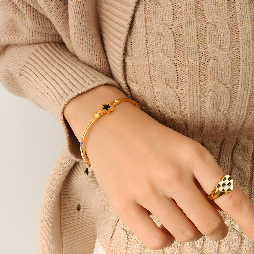 Bracelet jonc fin en titane plaqué or 18 carats avec étoile noire centrale, porté au poignet féminin.