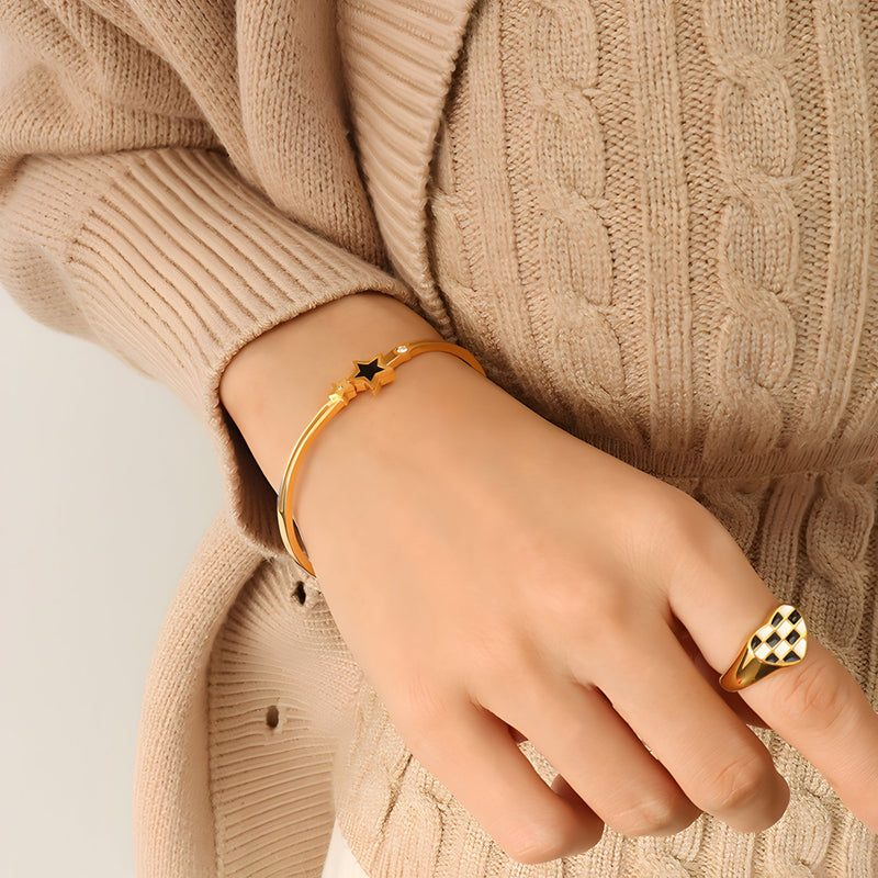 Bracelet jonc fin en titane plaqué or 18 carats avec étoile noire centrale, porté au poignet féminin.