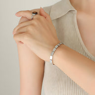 Bracelet fin en titane plaqué or 18 carats à maillons rectangulaires porté au poignet féminin.