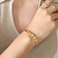 Bracelet en titane plaqué or 18 carats à maillons carrés modernes porté au poignet féminin.