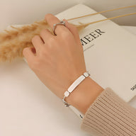 Bracelet fin en titane plaqué or 18 carats avec plaque gravée, porté au poignet, style moderne et épuré.