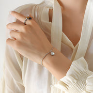 Bracelet fin en titane plaqué or 18 carats avec médaillon rond gravé « Lucky » porté au poignet féminin.