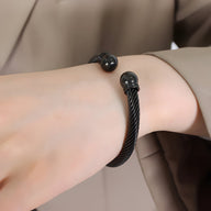 Bracelet rigide en titane noir avec extrémités sphériques lisses en plaqué or noir, style minimaliste.