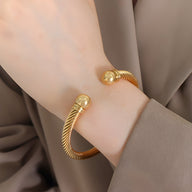 Bracelet rigide en titane plaqué or 18 carats à texture torsadée, extrémités sphériques lisses.