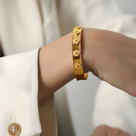 Bracelet jonc en titane plaqué or avec motifs fleurs en relief porté au poignet.