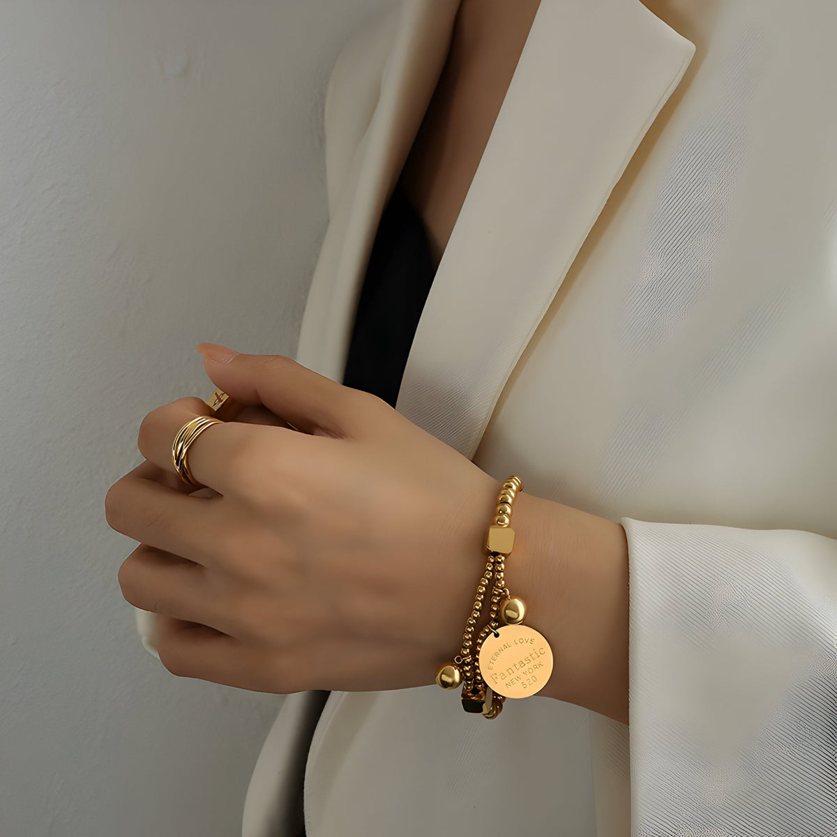Bracelet en titane doré avec perles rondes et médaillon gravé, porté au poignet féminin.