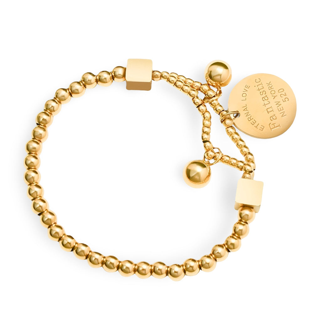 Bracelet en titane plaqué or avec perles dorées, médaillon gravé et fermoir coulissant.