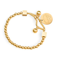 Bracelet en titane plaqué or avec perles dorées, médaillon gravé et fermoir coulissant.