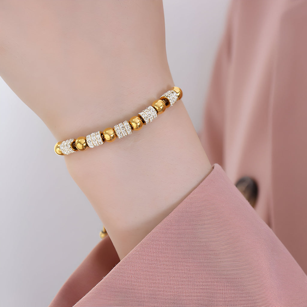 Bracelet en titane plaqué or avec perles dorées et pierres de cristal sur poignet féminin, style délicat.