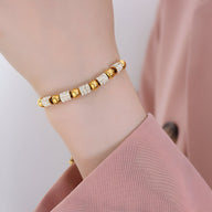 Bracelet en titane plaqué or avec perles dorées et pierres de cristal sur poignet féminin, style délicat.