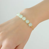 Bracelet or en titane avec cinq pierres épaisses de jade vert pâle, style Emma, porté au poignet féminin.