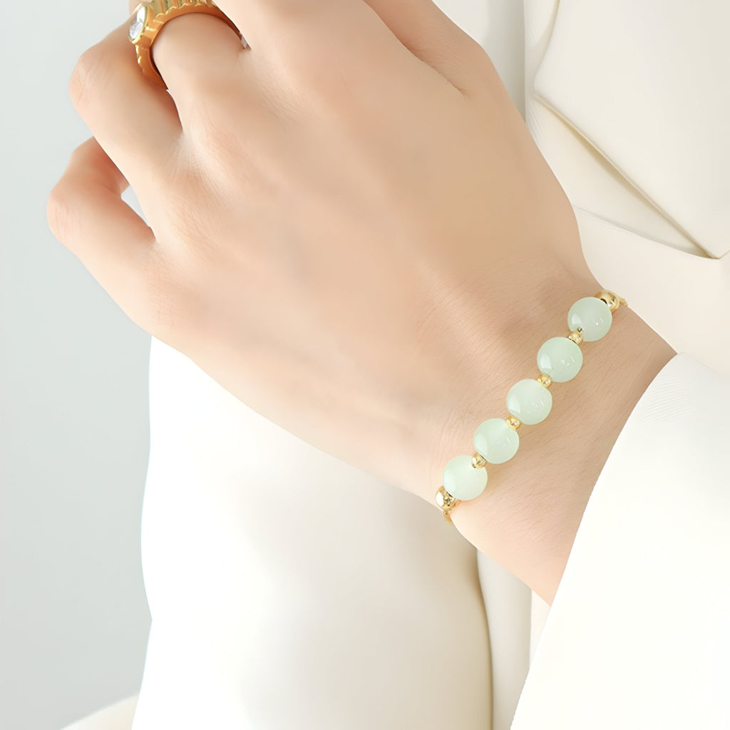 Bracelet doré en titane avec seven pierres épaisses de jade vert pâle sur poignet féminin.