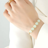 Bracelet doré en titane avec seven pierres épaisses de jade vert pâle sur poignet féminin.