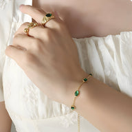 Bracelet doré en titane avec pierres de zircon vert imitation émeraude, style délicat et élégant.