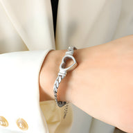 Bracelet en titane plaqué argent en maille avec motif cœur ouvert, style Sina, porté au poignet.