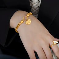 Bracelet en titane plaqué or à maille torsadée avec pendentif cœur brillant porté au poignet.