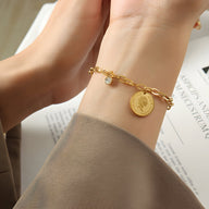 Bracelet chaîne doré en titane, médaillon Elisabeth II et pierre de zircon sur poignet féminin.