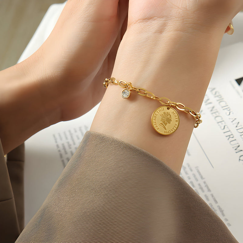 Bracelet chaîne doré en titane, médaillon Elisabeth II et pierre de zircon sur poignet féminin.