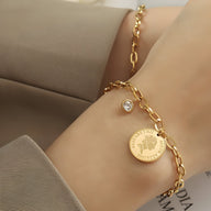 Bracelet en titane plaqué or avec maillons ovales, médaillon Elisabeth II gravé et zircon serti sur chaîne fine.